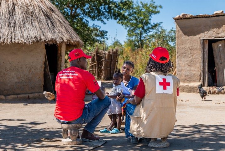 Red Crossers wearing vests crouch with a parent and child